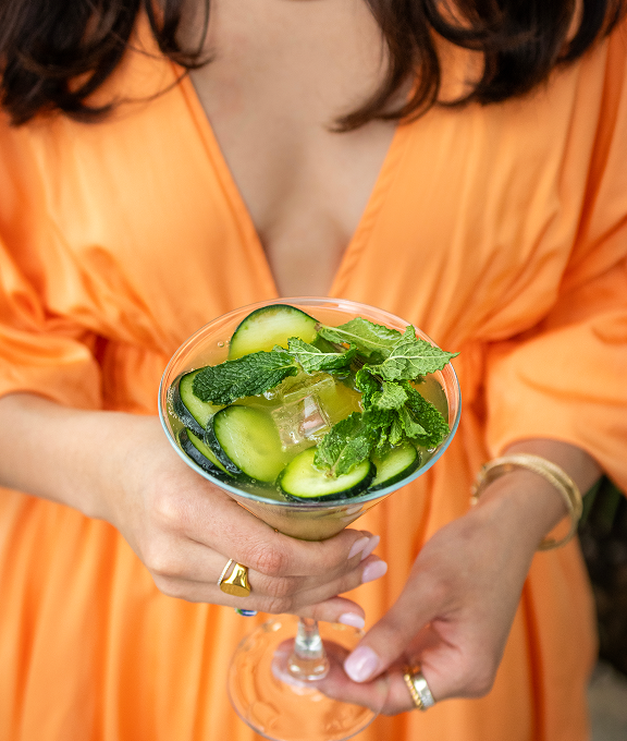 Woman in an orange dress holds a refreshing cucumber cocktail made with best vodka for cocktails